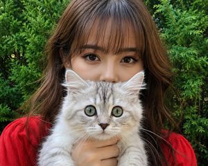 Woman with Kitten Close-up — A close-up, eye-level shot of a young woman with long, wavy brown hair and front bangs holding up a {argument name="kitten color" d