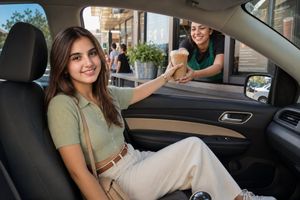 Sunny Drive-Thru Iced Coffee Portrait — Create a realistic DSLR-style candid photo from inside the front passenger seat of a car at a sunny drive-thru café. A s
