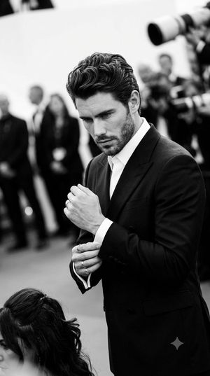 Monochromatic Red Carpet Tuxedo Portrait — A {argument name="subject" default="man"} stands centrally composed in a medium shot, his body angled in a 45 degree 