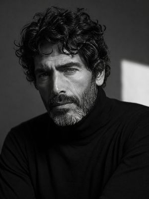 Rugged Masculine B&W Portrait — A cinematic black-and-white close-up portrait of a rugged, mature man with thick, naturally curly dark hair, strong masculine fa