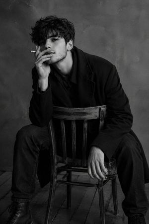 Moody Monochrome Male Portrait — Scene Description and Camera Angle
An intimate indoor portrait of a man sitting on a wooden chair turned backward, with the bac