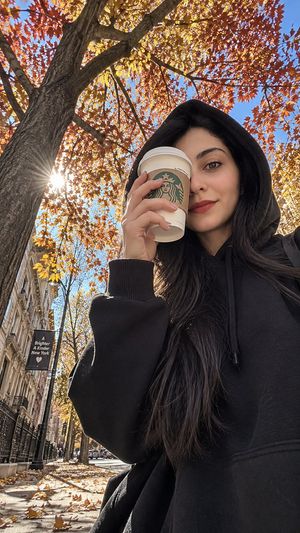 iPhone Street Style Autumn Hoodie Portrait — Create a **photorealistic autumn street-style photograph** captured from an extremely low, ground-level angle, look